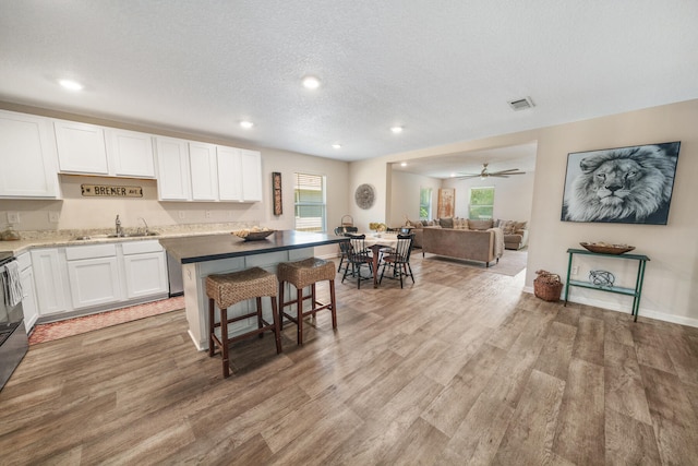 kitchen featuring ceiling fan, sink, a kitchen bar, white cabinetry, and light hardwood / wood-style floors