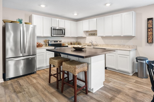 kitchen featuring hardwood / wood-style floors, appliances with stainless steel finishes, a kitchen bar, and white cabinetry