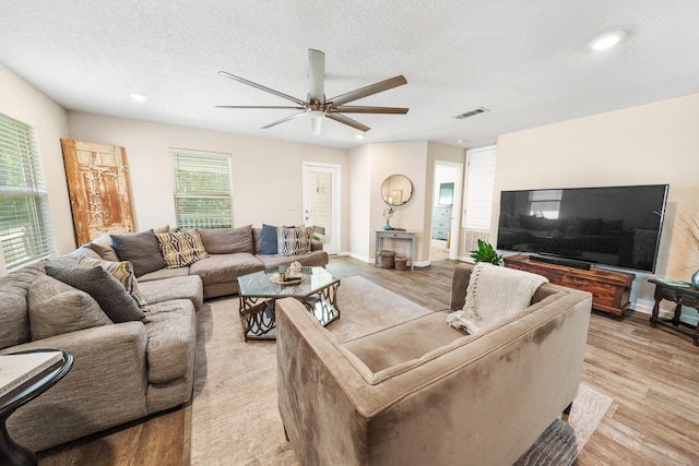 living room with ceiling fan, a textured ceiling, and light hardwood / wood-style floors