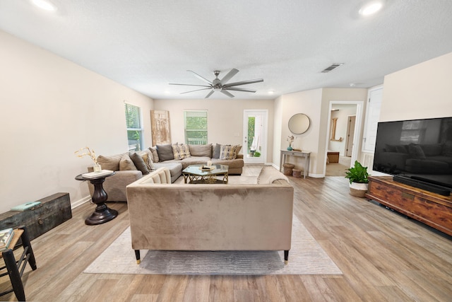 living room featuring light wood-type flooring, ceiling fan, and a textured ceiling