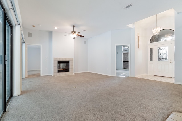 unfurnished living room featuring a tiled fireplace, a towering ceiling, light carpet, and ceiling fan with notable chandelier