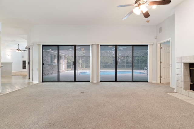 unfurnished living room featuring a tiled fireplace, light carpet, and ceiling fan