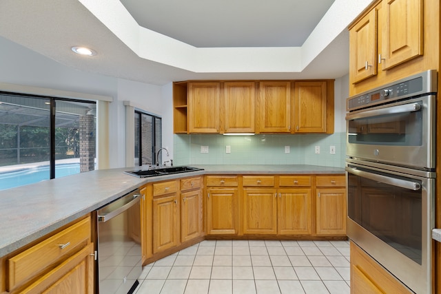 kitchen with stainless steel appliances, sink, kitchen peninsula, tasteful backsplash, and a raised ceiling