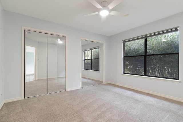 unfurnished bedroom featuring multiple closets, light colored carpet, and ceiling fan