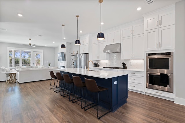 kitchen with ceiling fan, white cabinets, an island with sink, decorative light fixtures, and appliances with stainless steel finishes