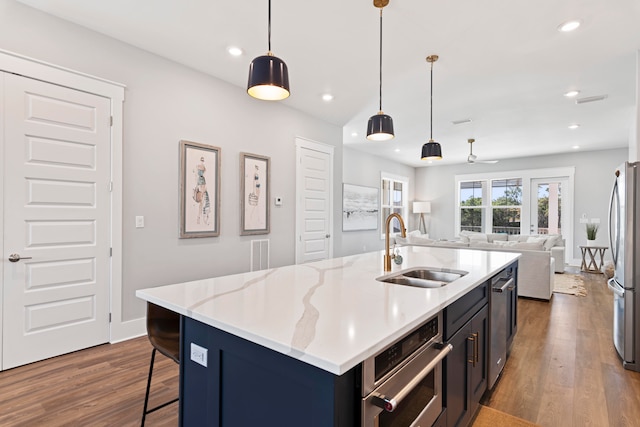 kitchen with dark wood-type flooring, stainless steel appliances, decorative light fixtures, a center island with sink, and sink