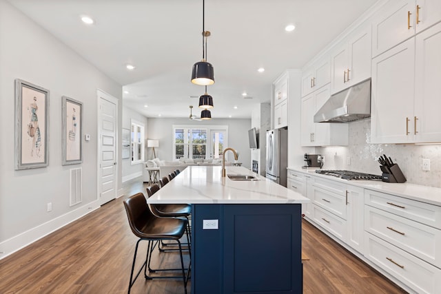 kitchen with appliances with stainless steel finishes, an island with sink, pendant lighting, dark hardwood / wood-style floors, and sink