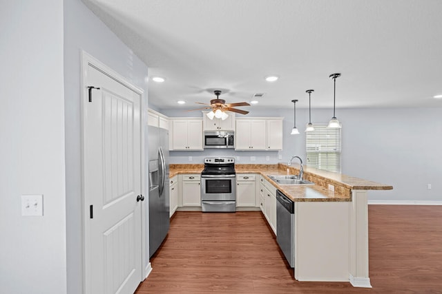 kitchen featuring appliances with stainless steel finishes, kitchen peninsula, hardwood / wood-style floors, and hanging light fixtures