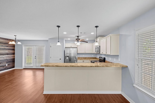 kitchen with dark hardwood / wood-style floors, wooden walls, kitchen peninsula, pendant lighting, and appliances with stainless steel finishes