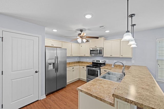 kitchen featuring kitchen peninsula, stainless steel appliances, sink, decorative light fixtures, and light hardwood / wood-style floors