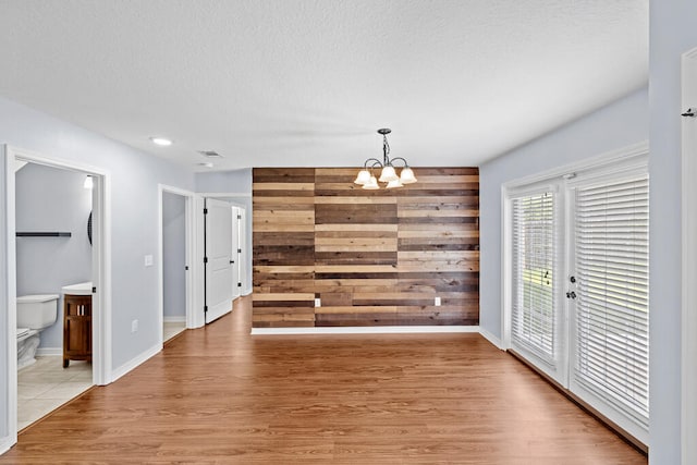 unfurnished dining area featuring light hardwood / wood-style floors, a notable chandelier, and a textured ceiling