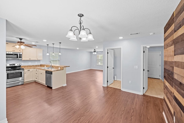 kitchen featuring wood-type flooring, sink, kitchen peninsula, stainless steel appliances, and decorative light fixtures