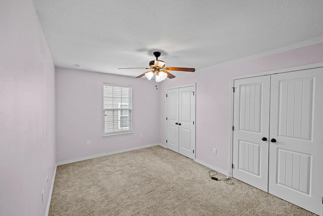 unfurnished bedroom featuring ceiling fan, light carpet, multiple closets, and a textured ceiling