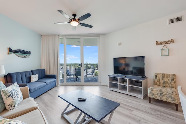 living room with ceiling fan, a wall of windows, and light hardwood / wood-style flooring