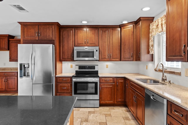 kitchen with appliances with stainless steel finishes, light stone counters, and sink