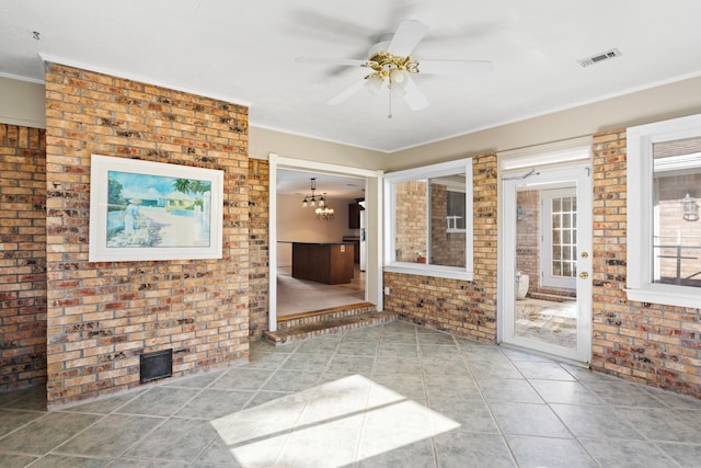 interior space featuring tile patterned flooring, ceiling fan with notable chandelier, and brick wall