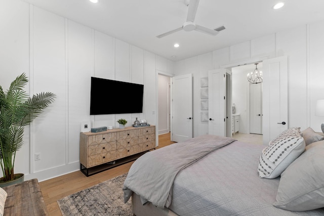 bedroom featuring ceiling fan with notable chandelier, connected bathroom, and light hardwood / wood-style floors