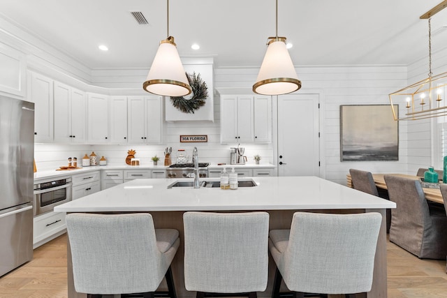 kitchen featuring hanging light fixtures, a kitchen island with sink, stainless steel appliances, and white cabinets