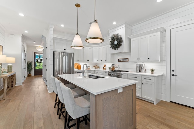 kitchen with white cabinetry, pendant lighting, stainless steel appliances, light wood-type flooring, and a center island with sink