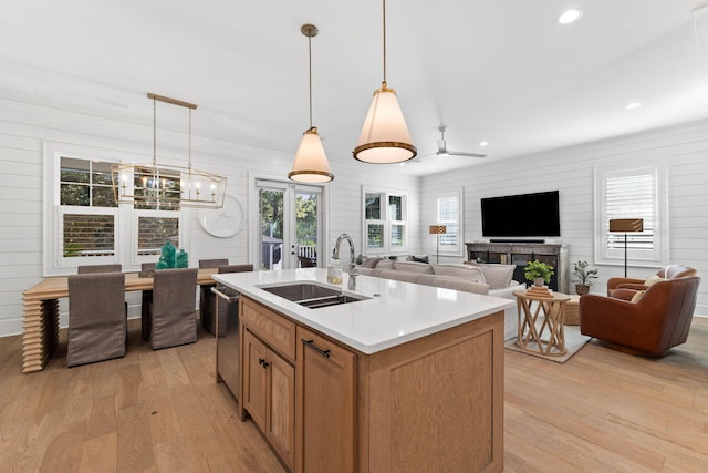 kitchen with pendant lighting, light wood-type flooring, stainless steel dishwasher, a kitchen island with sink, and sink