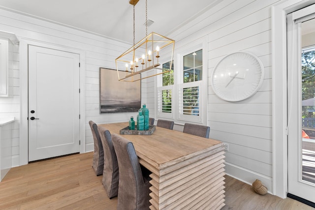 dining room with wooden walls, a chandelier, light hardwood / wood-style floors, and a healthy amount of sunlight