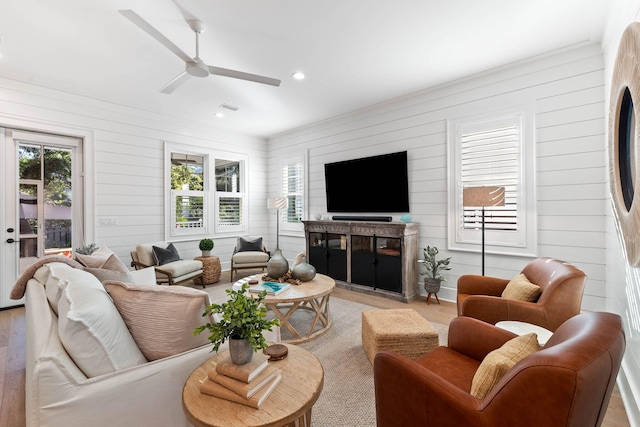 living room with light wood-type flooring, ceiling fan, and wooden walls