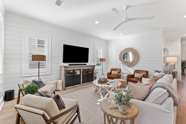 living room with ceiling fan, light wood-type flooring, and wood walls