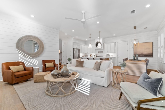 living room with ceiling fan, wooden walls, light hardwood / wood-style flooring, and ornamental molding