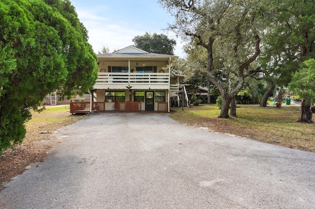 raised beach house with a carport, a front lawn, stairs, and aphalt driveway