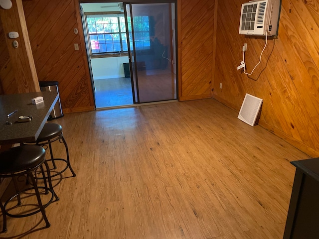 living room with a wall mounted AC, wooden walls, and light hardwood / wood-style flooring