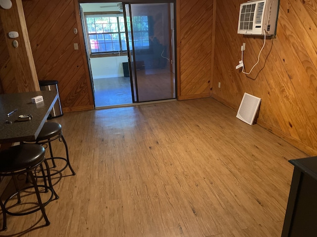 unfurnished dining area featuring an AC wall unit, baseboards, wood walls, and wood finished floors