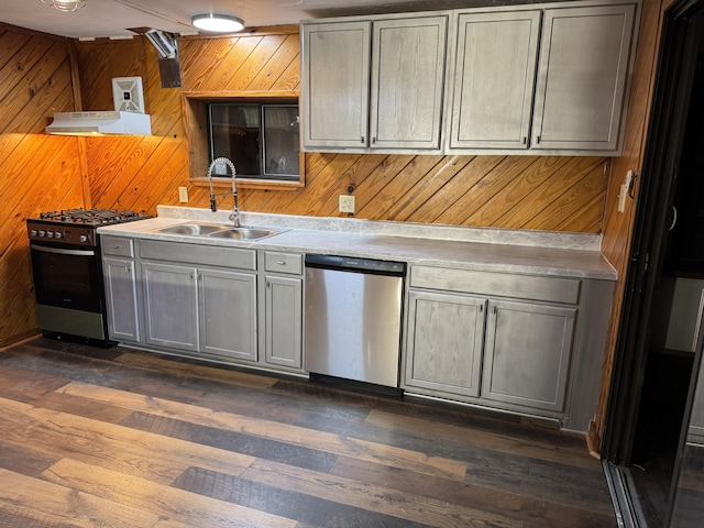 kitchen featuring gray cabinetry, sink, stainless steel appliances, and wood walls