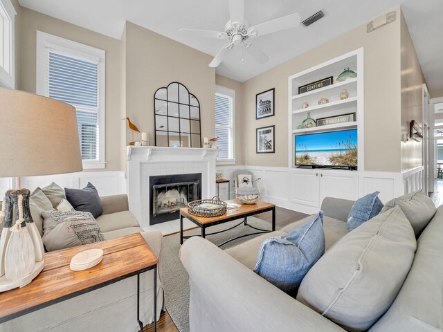 living room with a tiled fireplace, light hardwood / wood-style floors, built in features, and a wealth of natural light