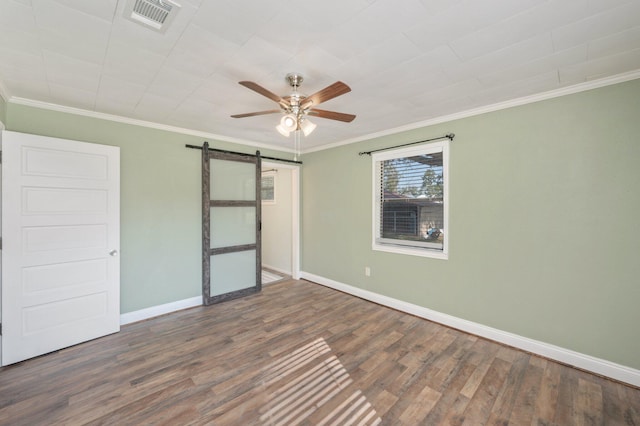 unfurnished bedroom with ornamental molding, ceiling fan, a barn door, and dark hardwood / wood-style floors