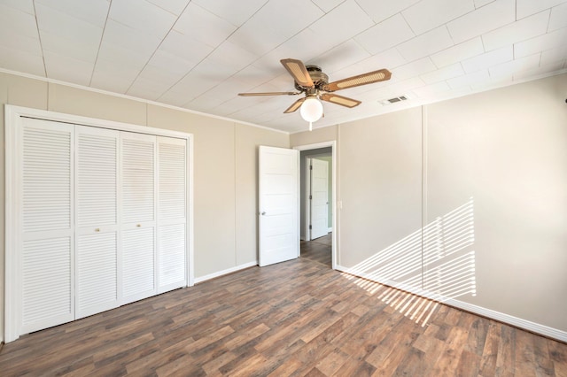 unfurnished bedroom with ceiling fan, a closet, crown molding, and dark wood-type flooring