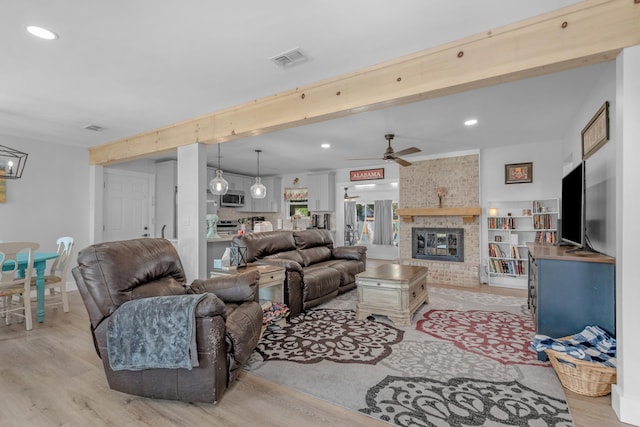 living room featuring a brick fireplace, beam ceiling, light hardwood / wood-style flooring, and ceiling fan