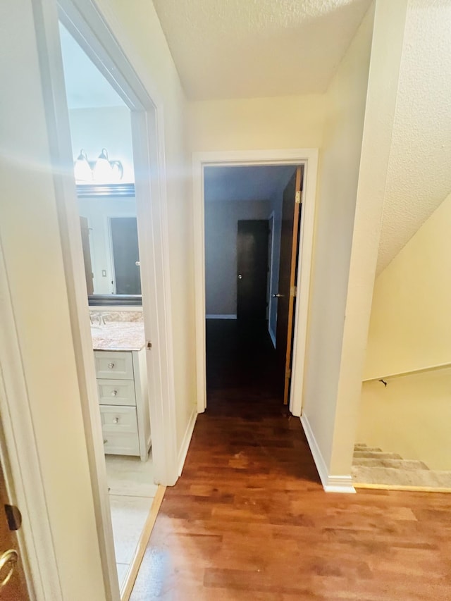 hallway featuring baseboards, a textured ceiling, and light wood-style flooring
