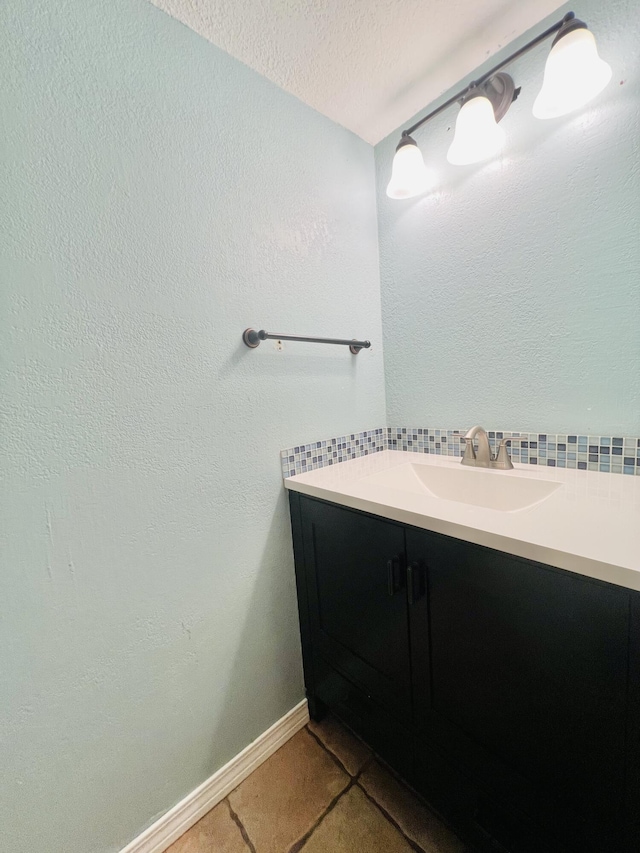bathroom with tile patterned flooring, vanity, a textured ceiling, baseboards, and decorative backsplash