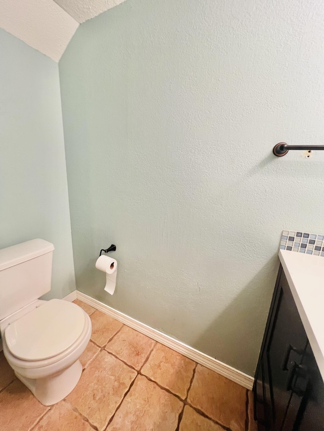 bathroom with vaulted ceiling, vanity, tile patterned floors, baseboards, and toilet