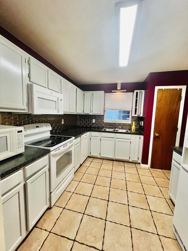 kitchen featuring dark countertops, a sink, white appliances, light tile patterned floors, and backsplash