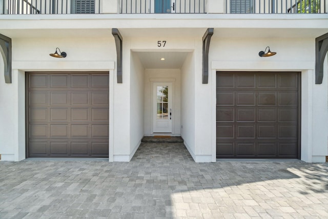 doorway to property featuring decorative driveway, an attached garage, a balcony, and stucco siding