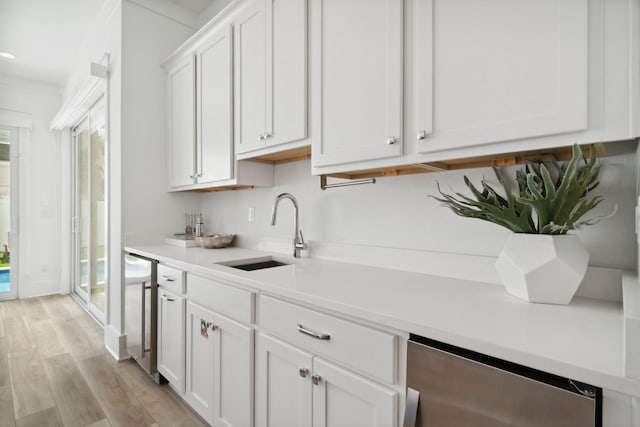 kitchen with sink, stainless steel dishwasher, beverage cooler, white cabinetry, and light wood-type flooring