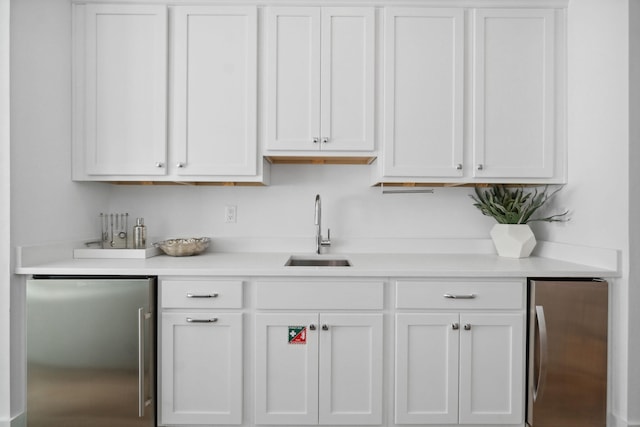 bar with white cabinetry, stainless steel fridge, and sink