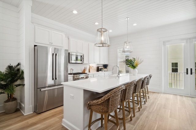 kitchen featuring light wood-style flooring, a breakfast bar, stainless steel appliances, light countertops, and white cabinetry