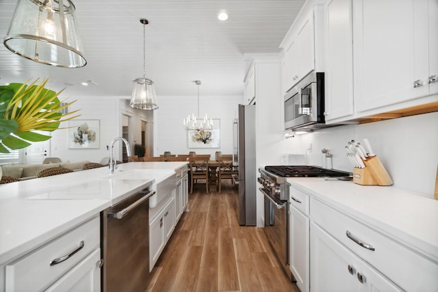 kitchen with stainless steel appliances, wood finished floors, white cabinets, light countertops, and decorative light fixtures