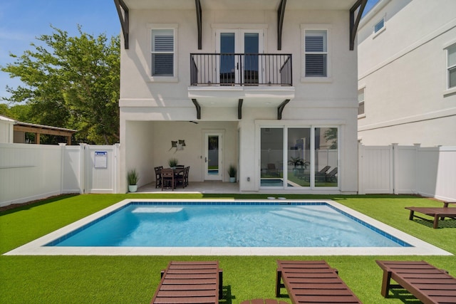 rear view of property with a balcony, a fenced backyard, a lawn, and stucco siding