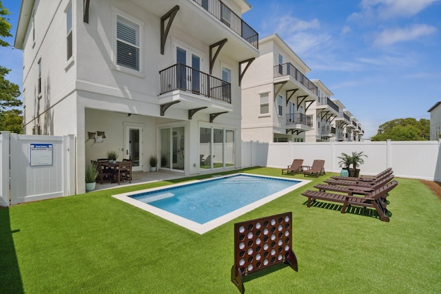 rear view of house featuring a fenced in pool, stucco siding, a lawn, a balcony, and a fenced backyard