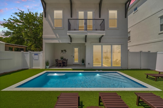 rear view of house with a fenced backyard, a lawn, a balcony, and stucco siding