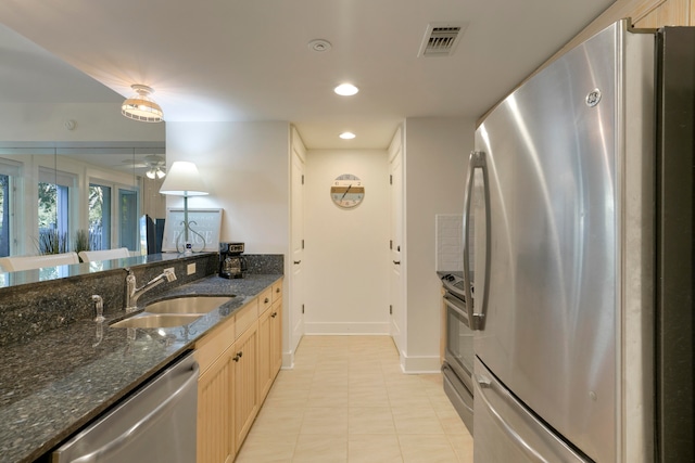 kitchen with stainless steel appliances, dark stone countertops, sink, pendant lighting, and light brown cabinetry