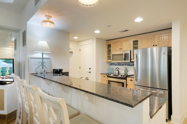 kitchen featuring decorative backsplash, stainless steel appliances, dark stone counters, and a breakfast bar